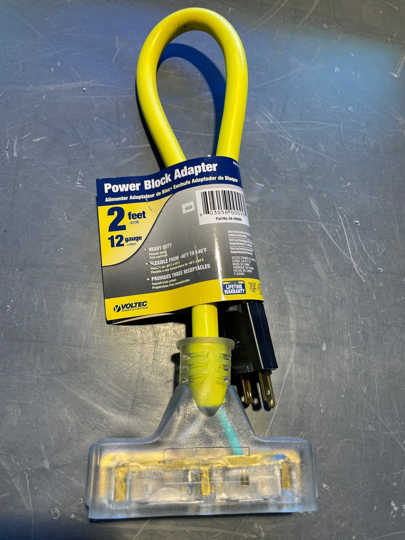 A yellow 2-foot power block adapter with a clear plastic ground clip on a scratched gray metal surface. The product has a blue and yellow retail paper label wrapped around the loop.