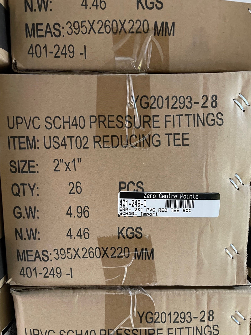 A close-up of stacked brown cardboard shipping boxes printed with product details for UPVC SCH40 pressure fittings, including item code US4T02 Reducing Tee, size 2"x1", quantity 26 pieces, and a Zero Centre Pointe label.