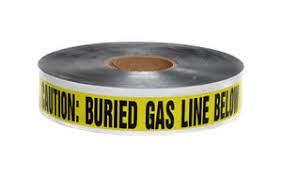 A roll of yellow detectable gas marking tape with text 'CAUTION: GAS LINE BELOW' printed on it, indicating the presence of buried gas lines.