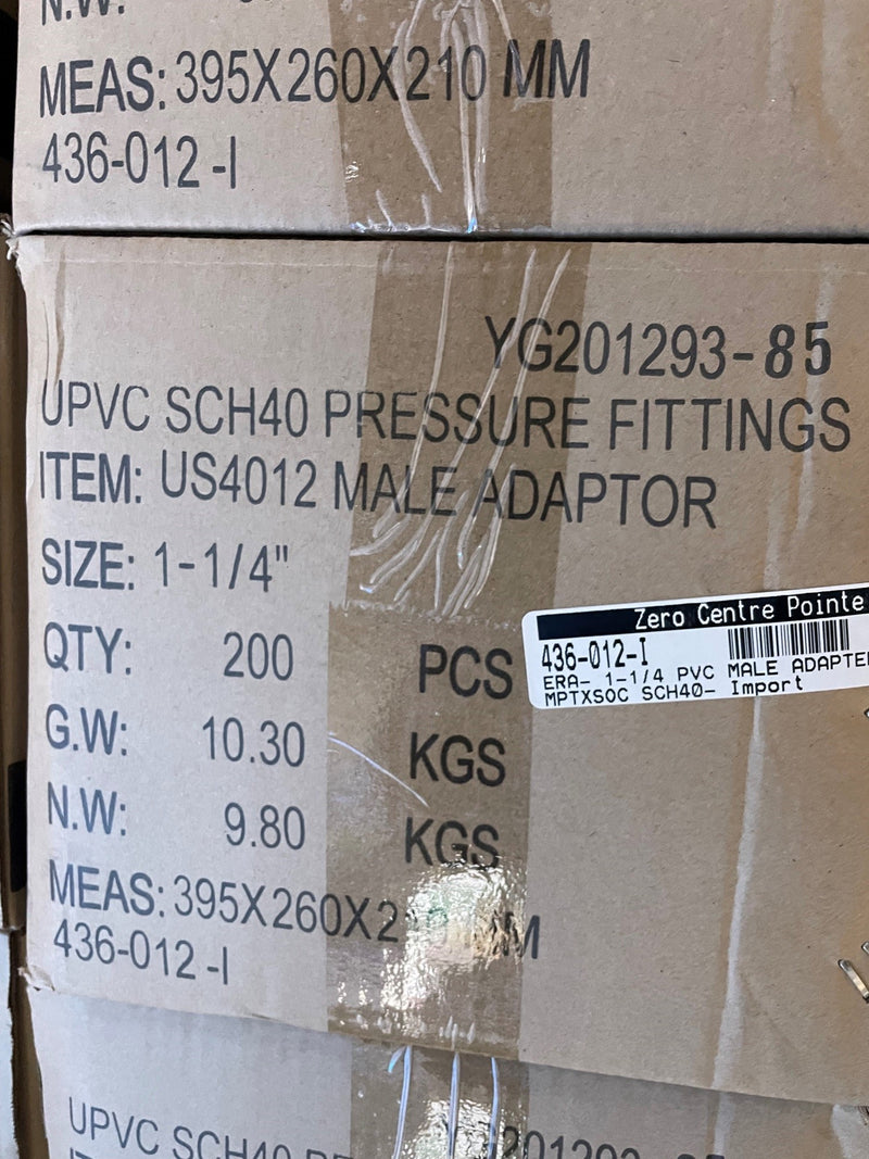 A close-up of stacked cardboard shipping boxes printed with product details for Upvc Sch40 Pressure Fittings, specifically a US4012 Male Adapter, with a Zero Centre Pointe label visible on the front.