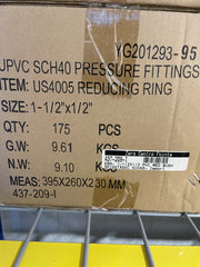 A cardboard shipping box for JPVC SCH40 pressure fittings, specifically a reducing ring, with printed specifications, a barcode label, and a yellow surface visible below.