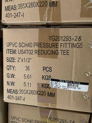 A close-up of stacked cardboard shipping boxes containing UPVC SCH40 pressure fittings, with printed product details including item number US4T02 REDUCING TEE, size 2" x 1/2", quantity 36 PCS, and weight information.