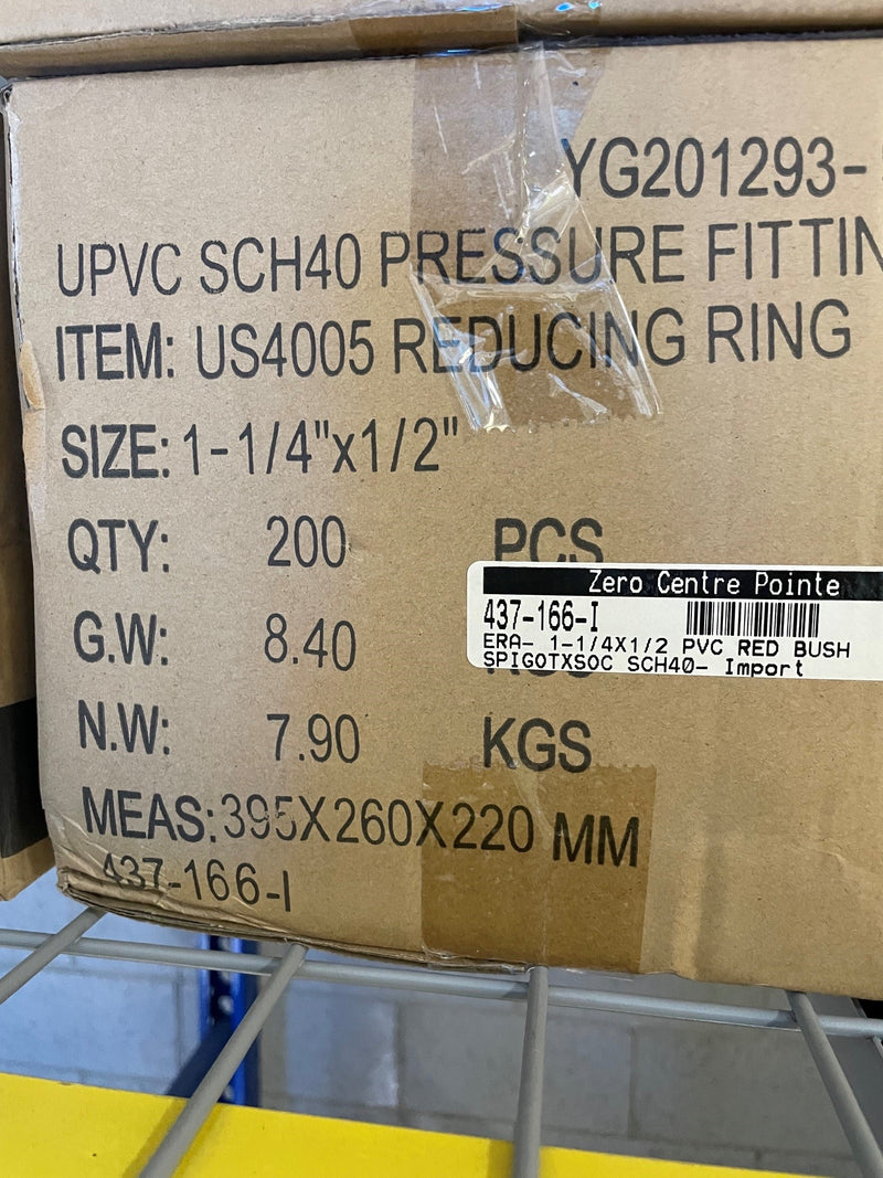 A brown cardboard box printed with product details for a UPVC SCH40 pressure fitting, item US4005 reducing ring, size 1-1/4 x 1/2, quantity 200 PCS, on a metal wire shelf.
