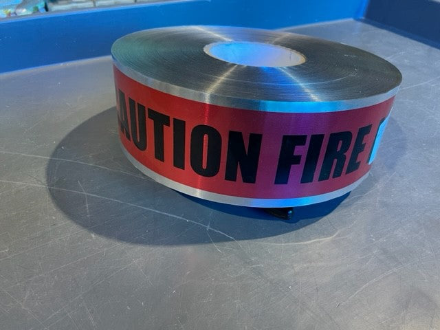 A roll of detectable red fire line marking tape with the words 'CAUTION FIRE LINE BELOW' printed on it.