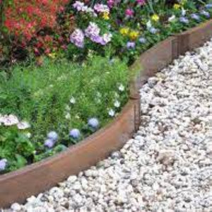 A redwood-colored bendable landscape edging board used to create a boundary around a garden bed with a variety of flowers behind it and a gravel pathway in front.