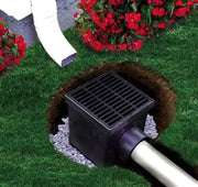 A black catch basin kit with a grate, placed in a garden setting.