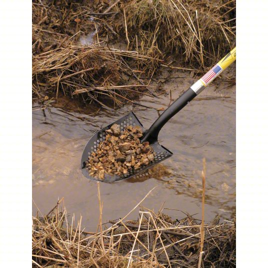 Shovel with a black handle holding rocks over water and dry grass.