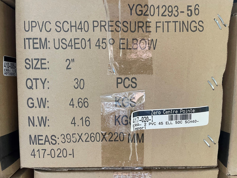 A close-up of a cardboard shipping box printed with product details for UPVC SCH40 pressure fittings, including item number US4E01 45° ELBOW, size 2 inches, quantity 30 PCS, and weight information. The box has tape closures and a barcode label.
