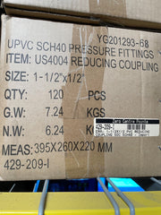 A cardboard shipping box for UPVC SCH40 pressure fittings, specifically reducing coupling item US4004, with printed specifications and a barcode label on a shelf.