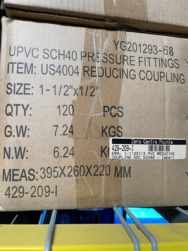 A cardboard shipping box for UPVC SCH40 pressure fittings, specifically reducing coupling item US4004, with printed specifications and a barcode label on a shelf.