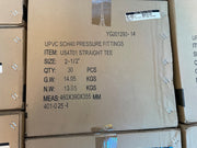 A large brown cardboard shipping box stacked on top of other boxes, printed with product details for UPVC SCH40 pressure fittings, item US4T01 straight tee, size 2-1/2 inches, quantity 30, gross weight 14.05 KGS, net weight 13.