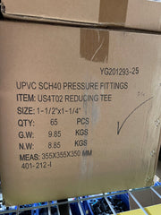 A close-up of a brown cardboard shipping box printed with product details for UPVC SCH40 pressure fittings, item US4T02 reducing tee, size 1-1/2" x 1-1/4", quantity 65 pieces.