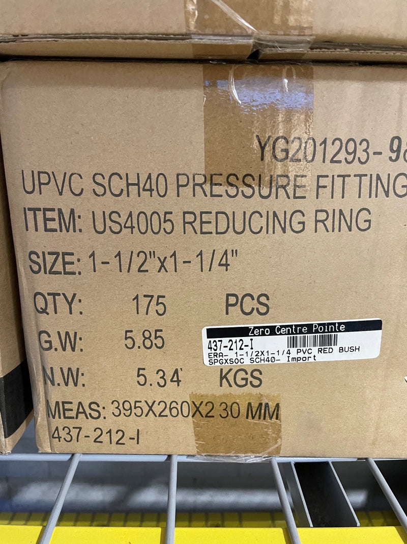 A close-up of a brown cardboard shipping box printed with product details for a US4005 reducing ring pressure fitting, including size, quantity, weight, and measurements. A barcode label is visible on the front of the box.