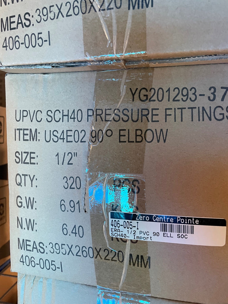 A close-up of stacked cardboard shipping boxes printed with product information for UPCVC SCH40 pressure fittings, specifically a 90-degree elbow, size 1/2 inch. The label includes item number US4E02, quantity 320, and weight details, with a clear tape strip across the middle.