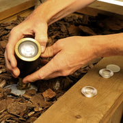 Person adjusting a small outdoor light fixture on wooden planks.
