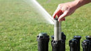 Person adjusting a sprinkler system on a grassy area