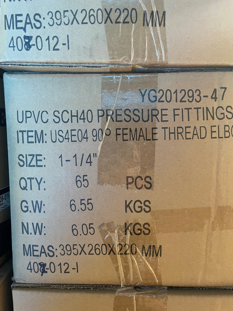 A close-up of stacked cardboard boxes printed with product details for UPVC SCH40 pressure fittings, including size, quantity, and weight information.