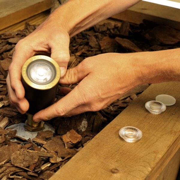 Person adjusting a small outdoor light fixture on wooden planks.