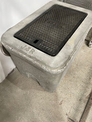A concrete valve box with a hinged cast iron lid.