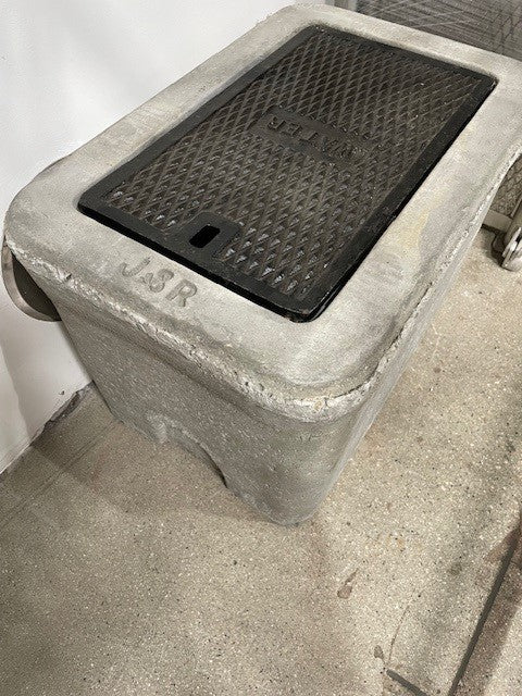 A concrete valve box with a hinged cast iron lid.