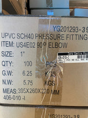 A close-up of a cardboard shipping box printed with product details for a UPVC SCH40 pressure fitting elbow, including item number US4E02, size 1 inch, quantity 100 pieces, weight details, and measurements. A black and white label from Zero Centre Point is visible on the front.