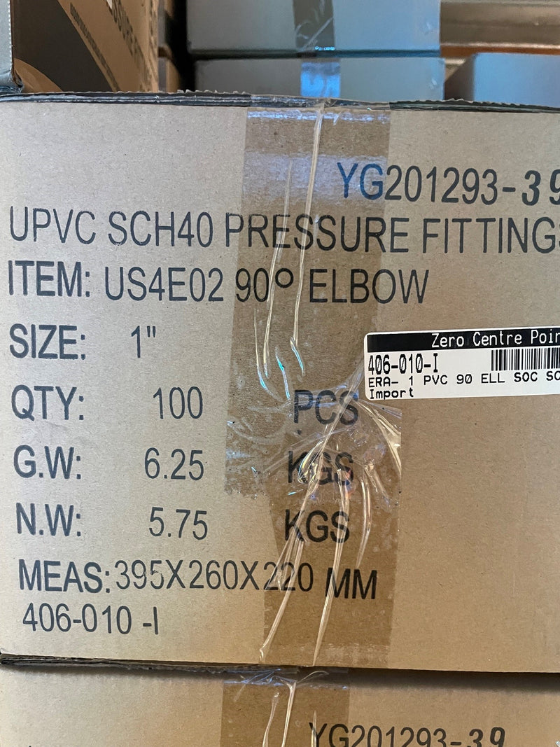 A close-up of a cardboard shipping box printed with product details for a UPVC SCH40 pressure fitting elbow, including item number US4E02, size 1 inch, quantity 100 pieces, weight details, and measurements. A black and white label from Zero Centre Point is visible on the front.