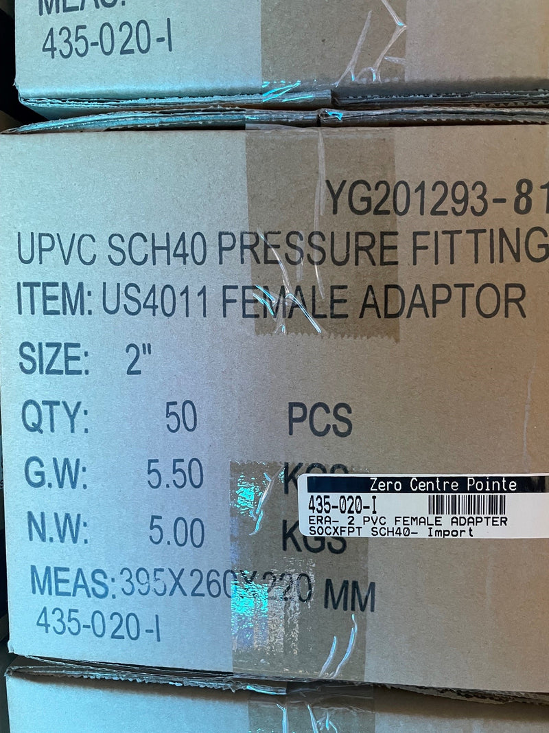 A close-up of stacked cardboard shipping boxes containing UPVC SCH40 pressure fittings, with printed text identifying the item as a female adapter, size 2 inch, quantity 50 pieces.