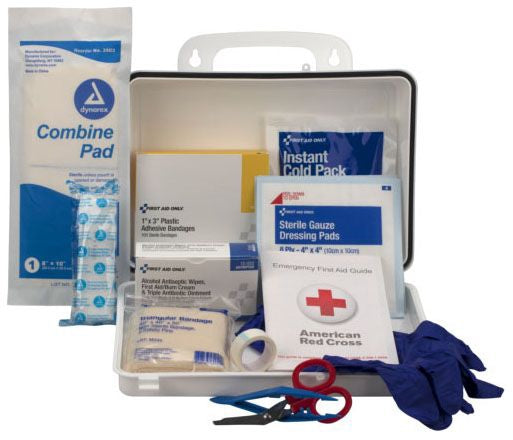 emergency first aid kit containing various medical supplies including bandages, an instant cold pack, sterile gauze dressing pads, an American Red Cross guide, blue gloves, and scissors, with a Synergy Combine Pad standing outside the kit.