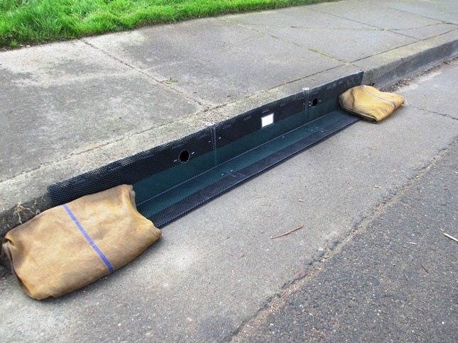 A black curb inlet protection device with a brown overlap, placed on a street curb.
