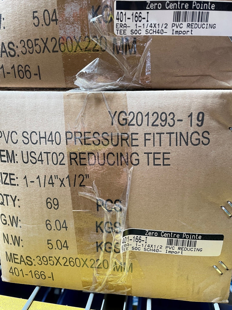 A close-up of stacked cardboard boxes containing PVC SCH40 pressure fittings, with printed labels and barcodes visible on the boxes.