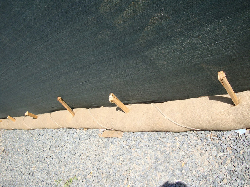 Long roll of brown paper or fabric with wooden stakes on a gravel surface.