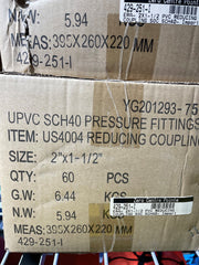 A close-up of a cardboard shipping box printed with product details for UPVC SCH40 pressure fittings, including size, quantity, gross weight, net weight, and measurements. Another similar box is partially visible above it.