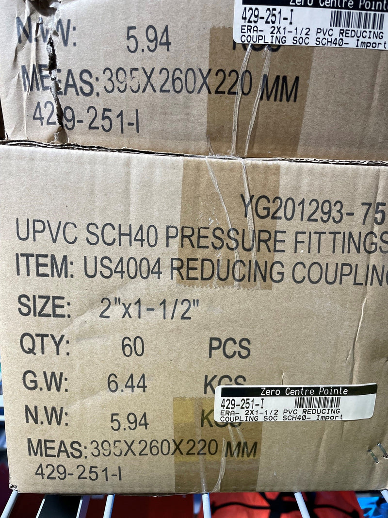 A close-up of a cardboard shipping box printed with product details for UPVC SCH40 pressure fittings, including size, quantity, gross weight, net weight, and measurements. Another similar box is partially visible above it.