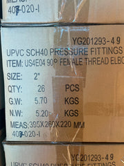 A close-up of stacked cardboard boxes containing UPVC SCH40 pressure fittings, with printed specifications including size 2 inches, quantity 26 pieces, and weight details.