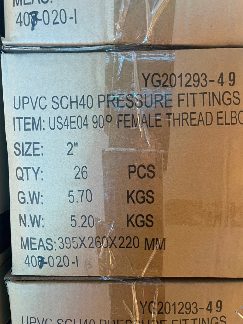 A close-up of stacked cardboard boxes containing UPVC SCH40 pressure fittings, with printed specifications including size 2 inches, quantity 26 pieces, and weight details.