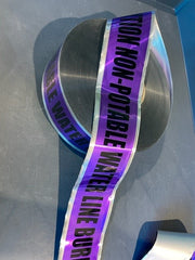 A roll of purple detectable marking tape with text 'NON-POTABLE WATER LINE BURIED BELOW' printed in black.