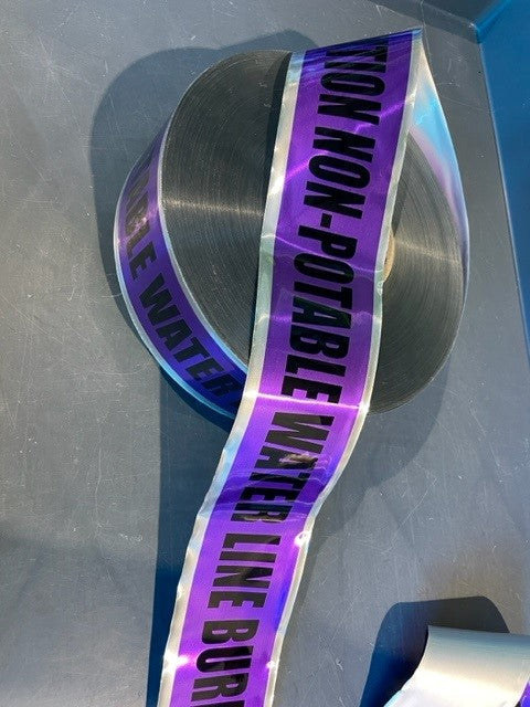 A roll of purple detectable marking tape with text 'NON-POTABLE WATER LINE BURIED BELOW' printed in black.