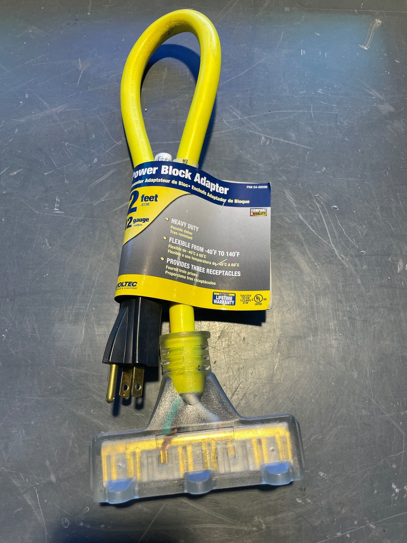 A yellow and black outdoor power block adapter with a 2-foot flexible cord and a clear plastic ground sleeve, shown with its retail paper band on a scratched dark gray metal surface.
