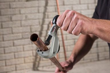 Person using a pipe cutter on a rusty pipe against a brick wall.