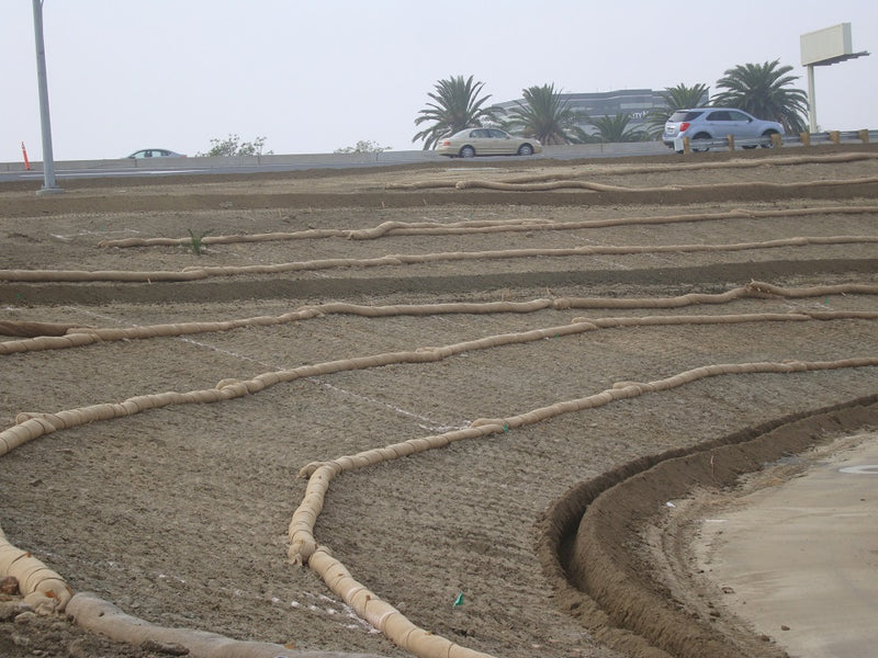 Dried-up riverbed with sand and ropes, cars on a road in the background