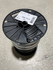 A spool of black irrigation wire on a concrete surface with a product label attached.