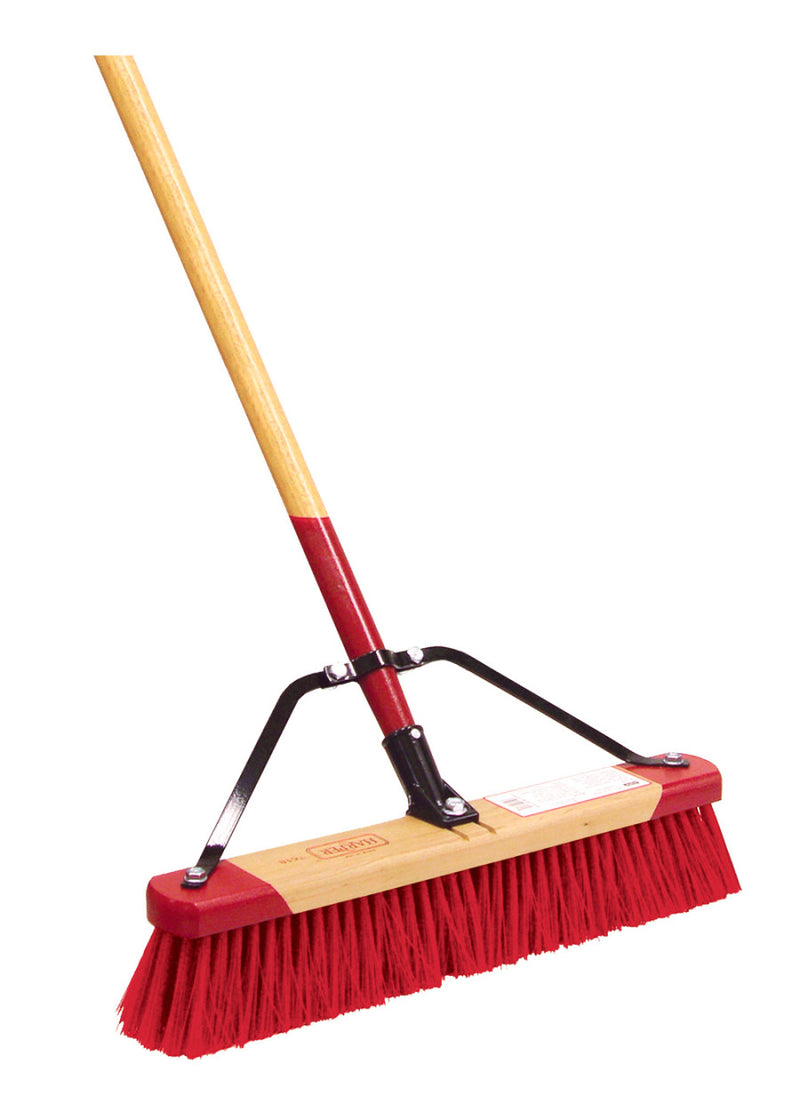 A push broom with a red and white bristle block attached to a wooden handle with a steel brace.