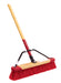 A push broom with a red and white bristle block attached to a wooden handle with a steel brace.