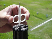 Hand holding a brass knuckle-shaped sprinkler head with grass in the background
