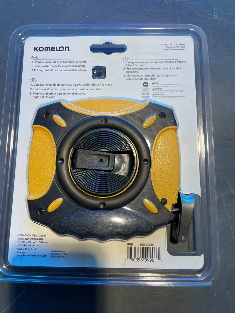 Komelon brand tape measure in its original blister packaging, featuring a black and yellow measuring device with a blue clip on a white backing card.