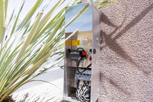 Electric meter box on a wall with plants in the foreground
