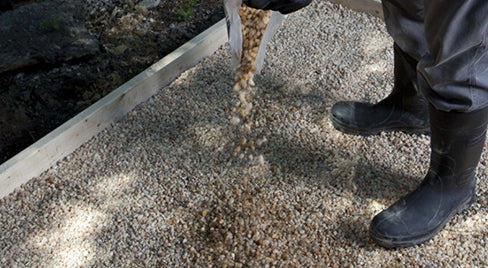 A person standing on a path made of Sakrete All Purpose 3/4" Gravel with boots raised slightly off the ground, showcasing the gravel's texture and color.