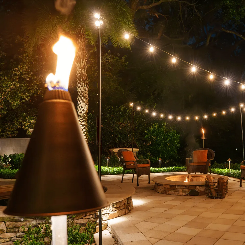 Outdoor patio with string lights, fire pit, and chairs at night.